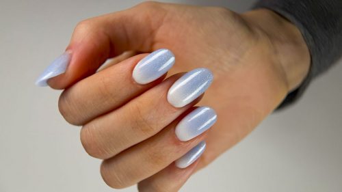 Nail extensions with white near the cuticle blending into a blue gradient and decorated with sparkling glitter dots.